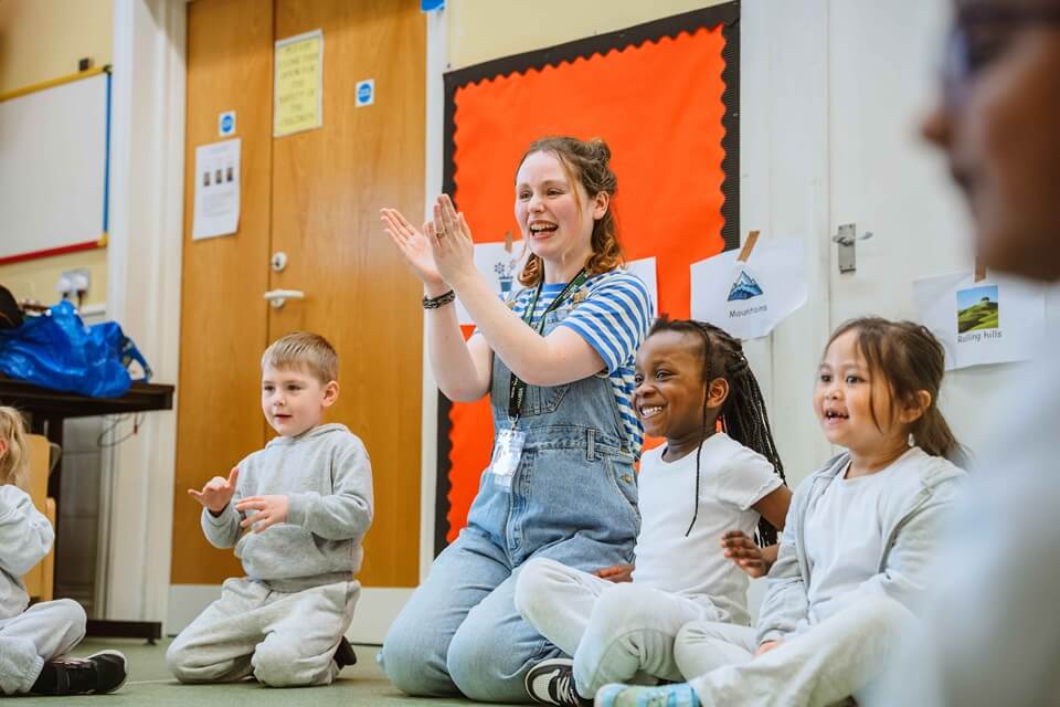 a group of young children seated with an adult clapping and sharing a story